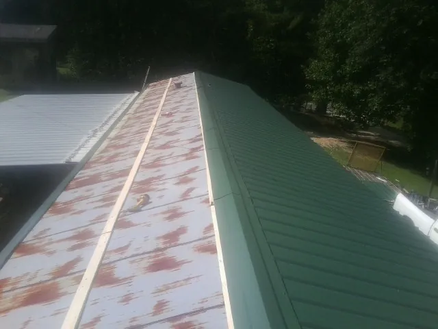 Old rusted panels beside newly installed green metal roofing — Wind Damage Roof Repair by Roofing Brothers in Welch