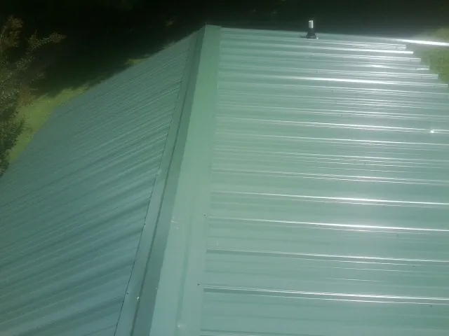 New green metal panels meeting at the ridge of a roof — Flat Roof Repair work by our crew in Welch