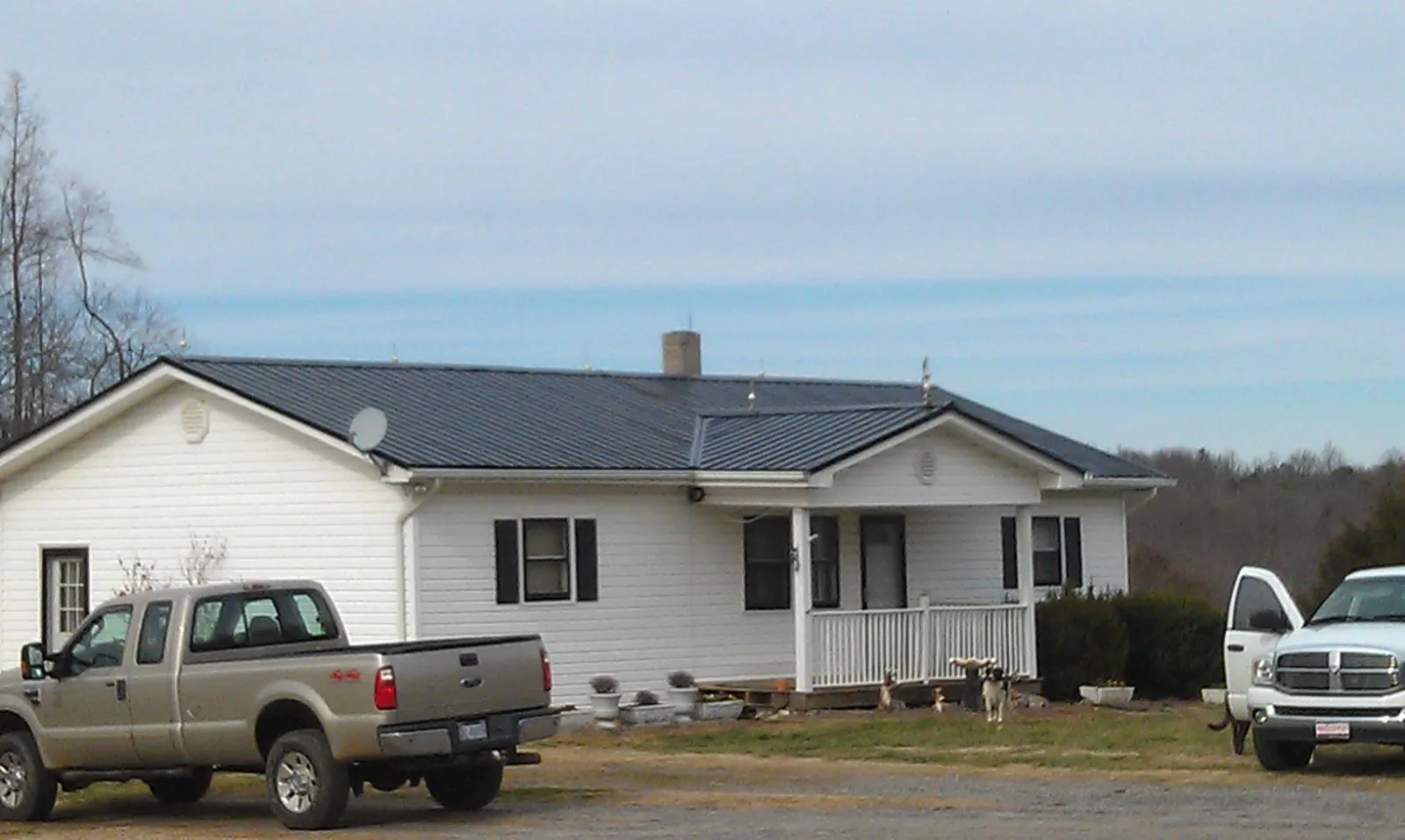 Finished dark metal roof on a white ranch home with work trucks parked in Welch