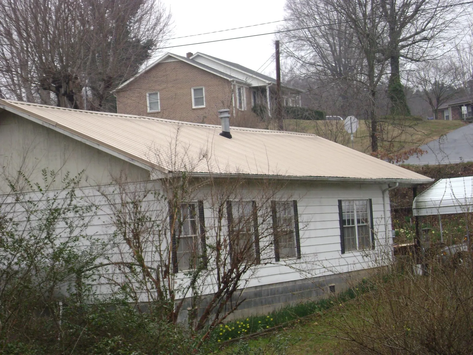 Tan metal roof on a white sided house set into a hillside — Commercial Roofing by Roofing Brothers in Welch